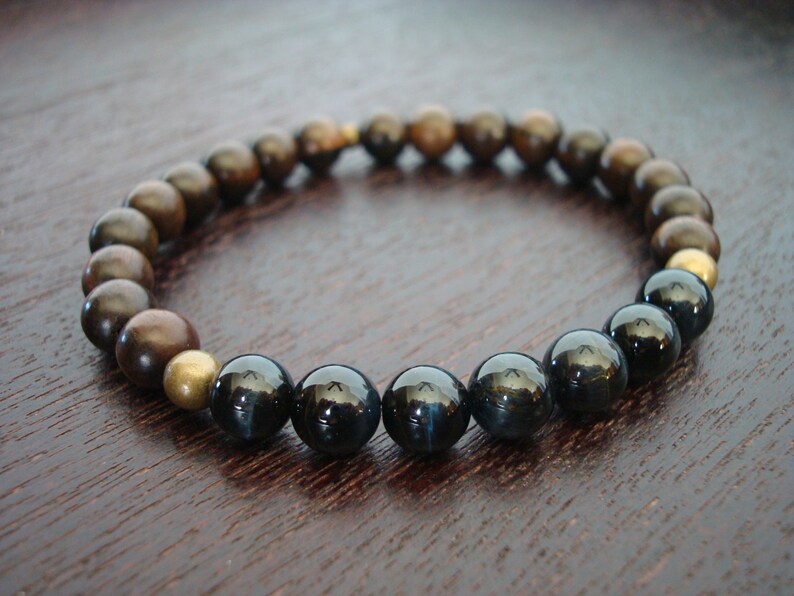 May include: A stretch bracelet with a mix of dark brown, bronze, and black beads. The bracelet features a few gold-coloured beads. The beads are round and smooth, creating a simple, elegant design.