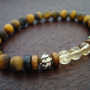 May include: A brown and gold beaded bracelet with a tiger's eye stone, clear quartz stones, and wooden beads with a white design.
