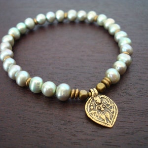 Puede incluir: Una pulsera de cuentas con perlas verde pálido y detalles dorados antiguos. La pulsera incluye un colgante decorativo con un diseño grabado. Las perlas tienen aproximadamente 8 mm de diámetro.