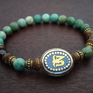 May include: A green and brown beaded bracelet with a silver and blue charm featuring a gold inscription.