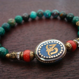 May include: A turquoise and red beaded bracelet with a silver and blue oval charm featuring a gold inscription.