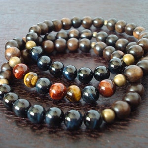 May include: Three beaded bracelets. The top bracelet features dark brown wooden beads. The middle bracelet has a mix of tiger eye, blue, and brown beads. The bottom bracelet has blue and brown beads. The beads are approximately 0.8 cm in diameter.