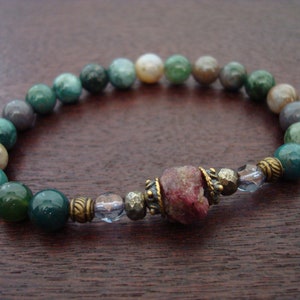 May include: A green, brown, and white agate gemstone bracelet with a pink ruby bead and gold accents.