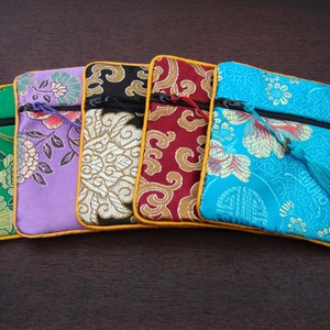 May include: Five decorative fabric pouches in various colours, each with a floral design. The pouches are green, purple, black, red, and turquoise, with gold trim and a zip. A tassel hangs from the turquoise pouch.