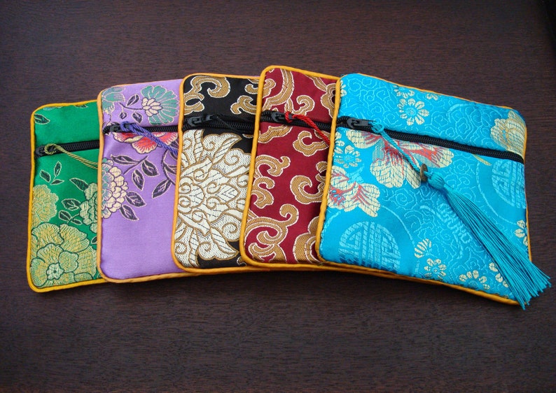May include: Five decorative fabric pouches in various colours, each with a floral design. The pouches are green, purple, black, red, and turquoise, with gold trim and a zip. A tassel hangs from the turquoise pouch.