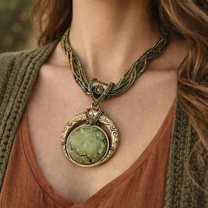 May include: A statement necklace featuring a large, round, green stone pendant set in a gold-toned frame. The necklace has a multi-strand braided design with green and gold beads. The pendant is suspended from a detailed clasp.