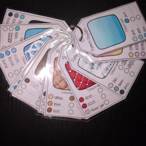 Puede incluir: Un anillo de tarjetas de muestras de color, cada una con un patrón y una paleta de colores únicos. Las tarjetas están etiquetadas con códigos y nombres de colores, y se utilizan para proyectos de diseño y arte. Las tarjetas están unidas a un anillo de metal plateado.