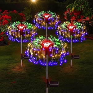 Può includere: Quattro luci solari da giardino con design a fuochi d'artificio. Ogni luce presenta un gruppo centrale di LED rossi e bianchi, circondato da luci verdi, gialle e blu. Le luci sono su pali di metallo con pannelli solari.