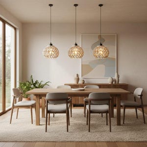 Peut inclure: Une salle à manger avec une table et des chaises en bois, éclairée par trois lampes suspendues avec des abat-jours décoratifs. La pièce comprend un buffet, une grande peinture et un tapis. Les lampes sont suspendues au plafond.