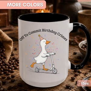 May include: A white ceramic mug with a black interior and handle, featuring a graphic of a white duck wearing a striped party hat and riding a silver scooter. The text above the duck reads, Off To Commit Birthday Crimes, in black font.