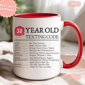 May include: A white ceramic mug with a red interior and handle, featuring the text 50 YEAR OLD TEXTING CODE and a list of humorous acronyms including ATD, BFF, BYOT, BTW, DWI, FWIW, GHA, ROFLACGU, OMSG, and TTYL with their definitions. The mug is 11oz.