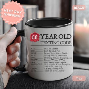 May include: A white ceramic mug with a black handle and rim, featuring the text 60 YEAR OLD TEXTING CODE and a list of humorous acronyms including ATD, BFF, BYOT, BTW, DWI, FWIW, GHA, ROFLACGU, OMSG, and TTYL. The mug is labeled as 11oz and black.