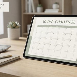 May include: A digital tablet displaying a 30-day challenge calendar with a grid layout. The screen shows the text 30-DAY CHALLENGE at the top. The tablet is positioned on a wooden surface next to a small notebook, a pen, and a calculator.
