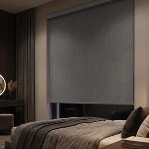 Könnte beinhalten: Ein dunkelgrauer Rollo-Schatten ist vor einem Schlafzimmerfenster heruntergelassen. Der Schatten besteht aus einem strukturierten Stoff. Das Bett hat eine graue Decke und Kissen. Ein dunkler Nachttisch aus Holz befindet sich neben dem Bett.