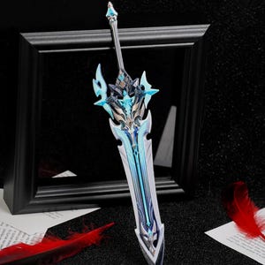 Puede incluir: Una espada de fantasía decorativa con una hoja plateada y una empuñadura azul y plateada intrincada. La espada se exhibe frente a un marco negro, con plumas rojas y papel impreso cerca.