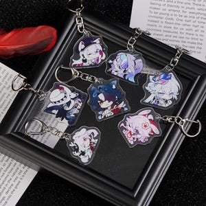 May include: A collection of seven acrylic keychains featuring anime-style character designs. Each keychain has a silver keyring and a detailed, colorful illustration of a character. The keychains are displayed on a black framed surface.