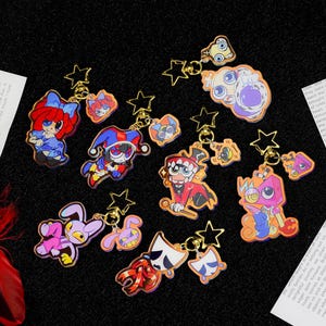 Puede incluir: Una colección de llaveros de acrílico coloridos con varios personajes de dibujos animados, incluyendo una figura de pelo rojo, un bufón, un conejo y un personaje enmascarado. Cada llavero incluye un cierre dorado en forma de estrella.