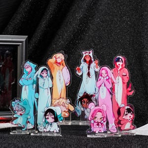 May include: Acrylic standees featuring anime-style characters in colorful pajamas. The standees depict various characters in different poses, with a range of colors including blue, pink, orange, and white. The standees are on clear bases.