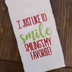May include: White kitchen towel with red and green embroidery that reads "I just like to smile smiling's my favorite!"