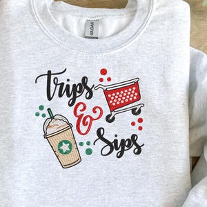 May include: Gray sweatshirt with embroidered text "Trips & Sips" and a red shopping cart with white polka dots. There is also an embroidered image of a coffee drink with whipped cream and a star.