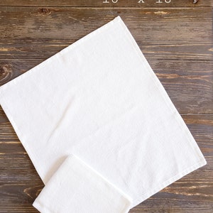 May include: Two white cotton bar mop towels, one folded on top of the other, on a brown wooden surface. The larger towel is 16 inches by 18 inches.