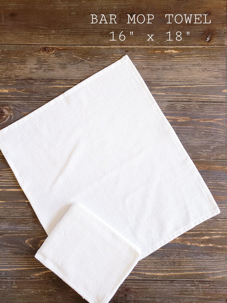 May include: Two white cotton bar mop towels, one folded on top of the other, on a brown wooden surface. The larger towel is 16 inches by 18 inches.