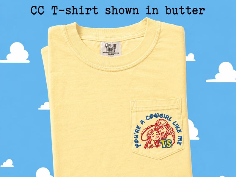 May include: A butter yellow short-sleeve t-shirt with a crew neckline and a chest pocket. The pocket features a graphic of two figures with the text "YOU'RE A COWGIRL LIKE ME" and "TS". The inner neck label reads "COMFORT COLORS". Text above reads "CC T-shirt shown in butter".