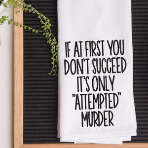 May include: White kitchen towel with black embroidered text that reads "If at first you don't succeed it's only "attempted" murder."
