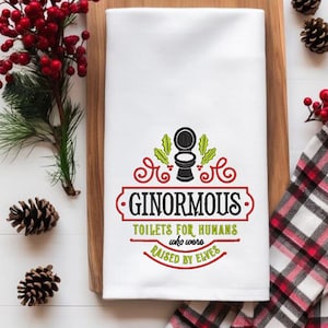 May include: White kitchen towel with red and green embroidery. The embroidery features a toilet with holly leaves and berries. The text reads "Ginormous Toilets for Humans who were raised by Elves."