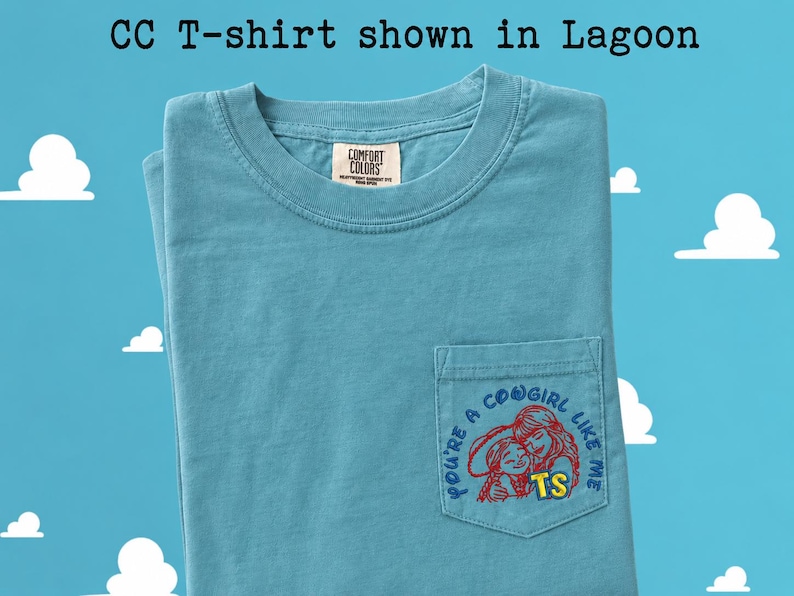 May include: A lagoon blue short-sleeve t-shirt with a chest pocket. The pocket features an embroidered graphic of two figures in red outlines with the blue text "YOU'RE A COWGIRL LIKE ME" and the yellow letters "TS". The neck label reads "COMFORT COLORS".