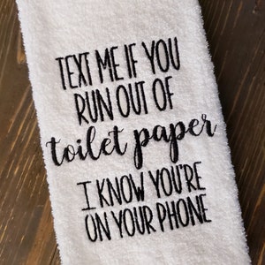 May include: White hand towel with black embroidered text that reads "Text me if you run out of toilet paper I know you're on your phone."