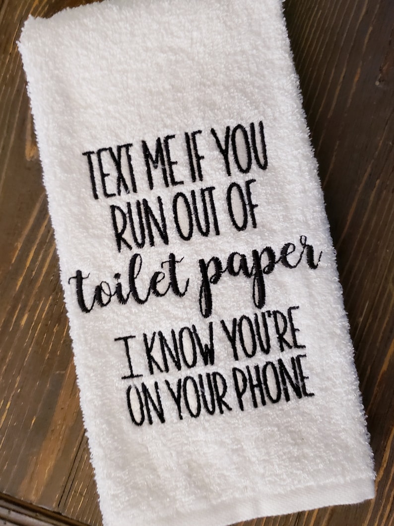 May include: White hand towel with black embroidered text that reads "Text me if you run out of toilet paper I know you're on your phone."