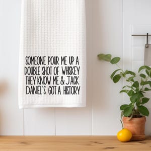 May include: White kitchen towel with black text that reads "Someone pour me up a double shot of whiskey they know me & Jack Daniel's got a history."