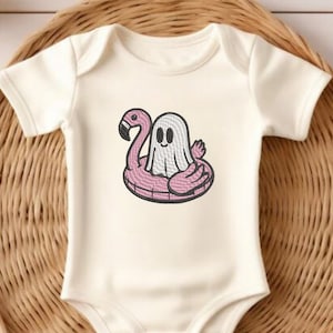Puede incluir: Body de bebé color crema con un diseño bordado de un fantasma de dibujos animados flotando en un flotador de piscina de flamenco rosa. El body tiene mangas cortas y un escote sencillo. El diseño está delineado en negro.