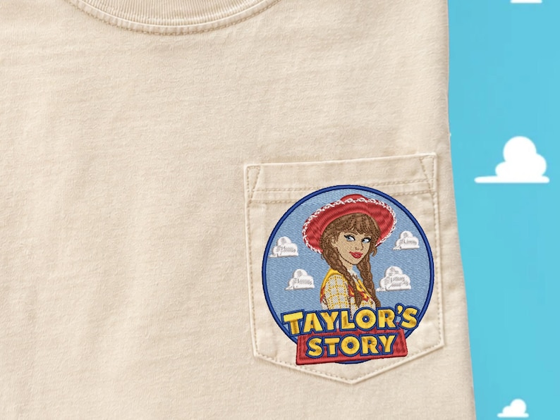 May include: A beige t-shirt with a chest pocket featuring an embroidered circular patch. The patch depicts a person with braided hair wearing a red cowgirl hat and yellow shirt, set against a blue sky with white clouds and the text Taylor's Story.