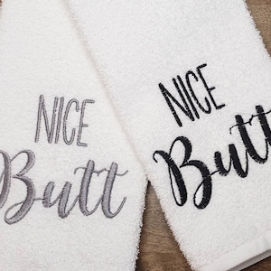 May include: Two white towels with the text "NICE BUTT" embroidered on them. One towel has the text in black and the other in gray.
