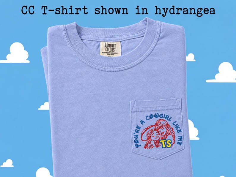 May include: A light purple short-sleeve t-shirt with a chest pocket. The pocket features a red and blue graphic of two figures with the text "YOU'RE A COWGIRL LIKE ME" and "TS". The inner neck label reads "COMFORT COLORS". Text above reads "CC T-shirt shown in hydrangea".