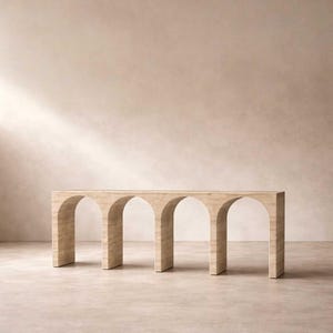 Può includere: Una consolle beige con un design ad arco. Il tavolo ha quattro arcate e un piano rettangolare. Il tavolo è realizzato in un materiale di pietra colorata e si trova su uno sfondo neutro.