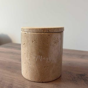 Peut inclure: Un récipient cylindrique beige avec un couvercle assorti. Le récipient a une surface texturée et le mot "May" est écrit sur le côté en cursive. Le récipient est posé sur une surface en bois.