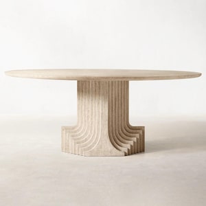 May include: A beige, round dining table with a unique pedestal base. The base features vertical and curved lines, creating a textured appearance. The table's top is a smooth, light beige color. The table is approximately 60 inches in diameter.