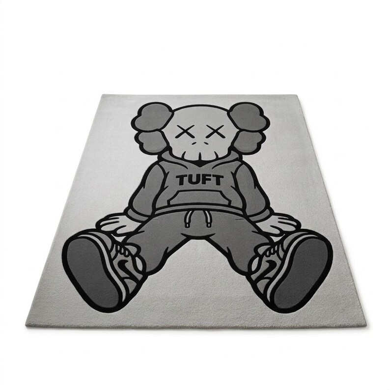 K&ouml;nnte beinhalten: Ein rechteckiger, hellgrauer Teppich mit einer Cartoonfigur in sitzender Position. Die Figur tr&auml;gt einen grauen Kapuzenpullover mit dem Wort "TUFT" auf der Vorderseite, eine graue Hose und graue Turnschuhe. Das Gesicht der Figur hat zwei "X" als Augen.