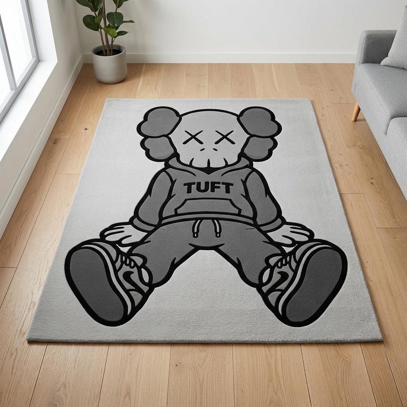 K&ouml;nnte beinhalten: Ein rechteckiger, grauer Teppich mit einer Cartoonfigur in sitzender Position. Die Figur tr&auml;gt einen grauen Kapuzenpullover mit dem Wort "TUFT", eine graue Hose und graue Turnschuhe. Das Gesicht der Figur hat "X" als Augen. Der Teppich liegt auf einem hellgrauen Boden.
