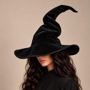May include: A black velvet witch hat with a tall, pointed, and slightly curved crown. The hat features a wide, flexible brim with a finished edge. The material has a soft, light-reflecting texture, and the design includes a distinct, slouchy peak.
