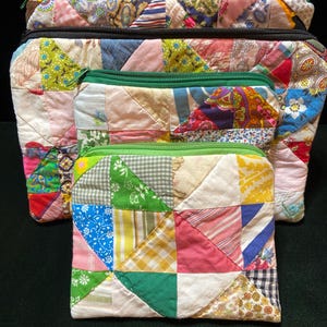 May include: Three rectangular zippered pouches of varying sizes, each constructed from a patchwork of assorted cotton fabrics in diverse colors and patterns, including floral, gingham, and striped prints, finished with green or black zipper closures.
