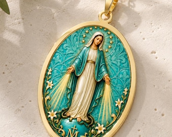 Puede incluir: Un colgante ovalado de oro con la imagen de la Virgen María vestida con túnica blanca y manto azul sobre un fondo turquesa. El diseño incluye rayos de luz, estrellas, lirios y la letra M con una cruz en la parte inferior.