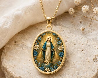 Puede incluir: Un collar con colgante ovalado en tono dorado que presenta una imagen central de la Virgen María de pie sobre un globo terráqueo, rodeada por un borde decorativo de flores azules y blancas. El colgante cuelga de una cadena de metal dorada.