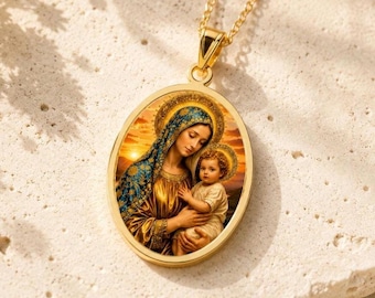 Puede incluir: Un collar con colgante ovalado en tono dorado que presenta una ilustración detallada a color de una mujer con un tocado azul y dorado sosteniendo a un niño pequeño. El colgante cuelga de una delicada cadena dorada con un motivo religioso.