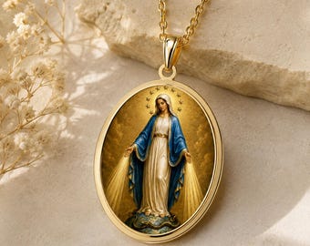 Puede incluir: Un colgante ovalado de tono dorado en una cadena a juego que muestra una representación detallada de la Virgen María con túnica blanca y manto azul, rodeada por un halo de estrellas y rayos de luz que emanan de sus manos extendidas.