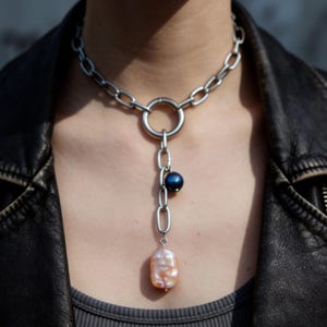 Puede incluir: Una taza de cerámica blanca con asa negra y el texto "But First, Coffee" en negrita negra. La taza se encuentra sobre un fondo borroso, sugiriendo un ambiente acogedor.