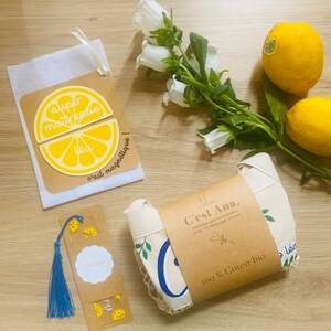 Può includere: Un set composto da una calamita gialla a forma di limone con il testo super maîtresse e Léa, un segnalibro rettangolare con una nappa blu e una borsa in cotone biologico piegata avvolta da una fascia di carta 100% Coton bio.